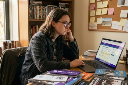 Jeune femme étudiante comparant des brochures d'écoles de cinéma sur son bureau encombré