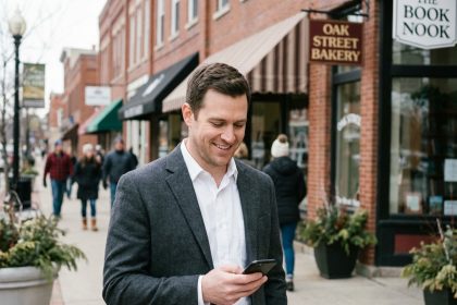 Homme souriant v&eacute;rifiant son t&eacute;l&eacute;phone en ville